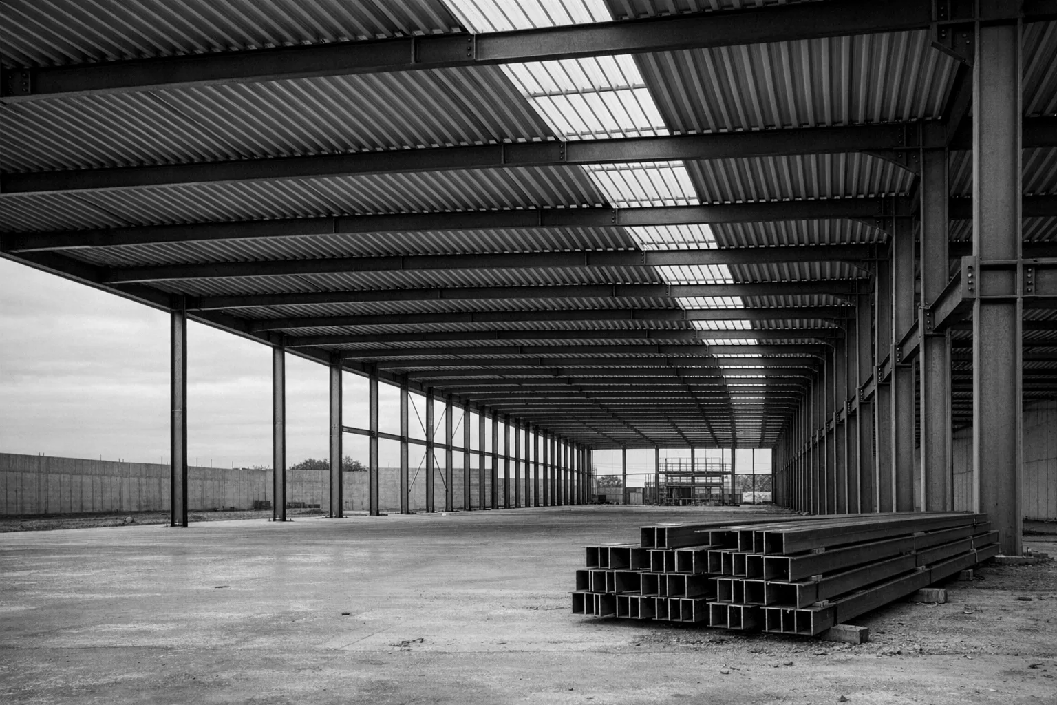 Ossature métallique d’un hall industriel en construction, en noir et blanc.